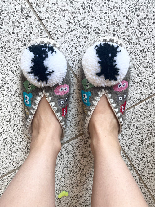 Pair of cartoonish shoes with pom-poms on a speckled floor.
